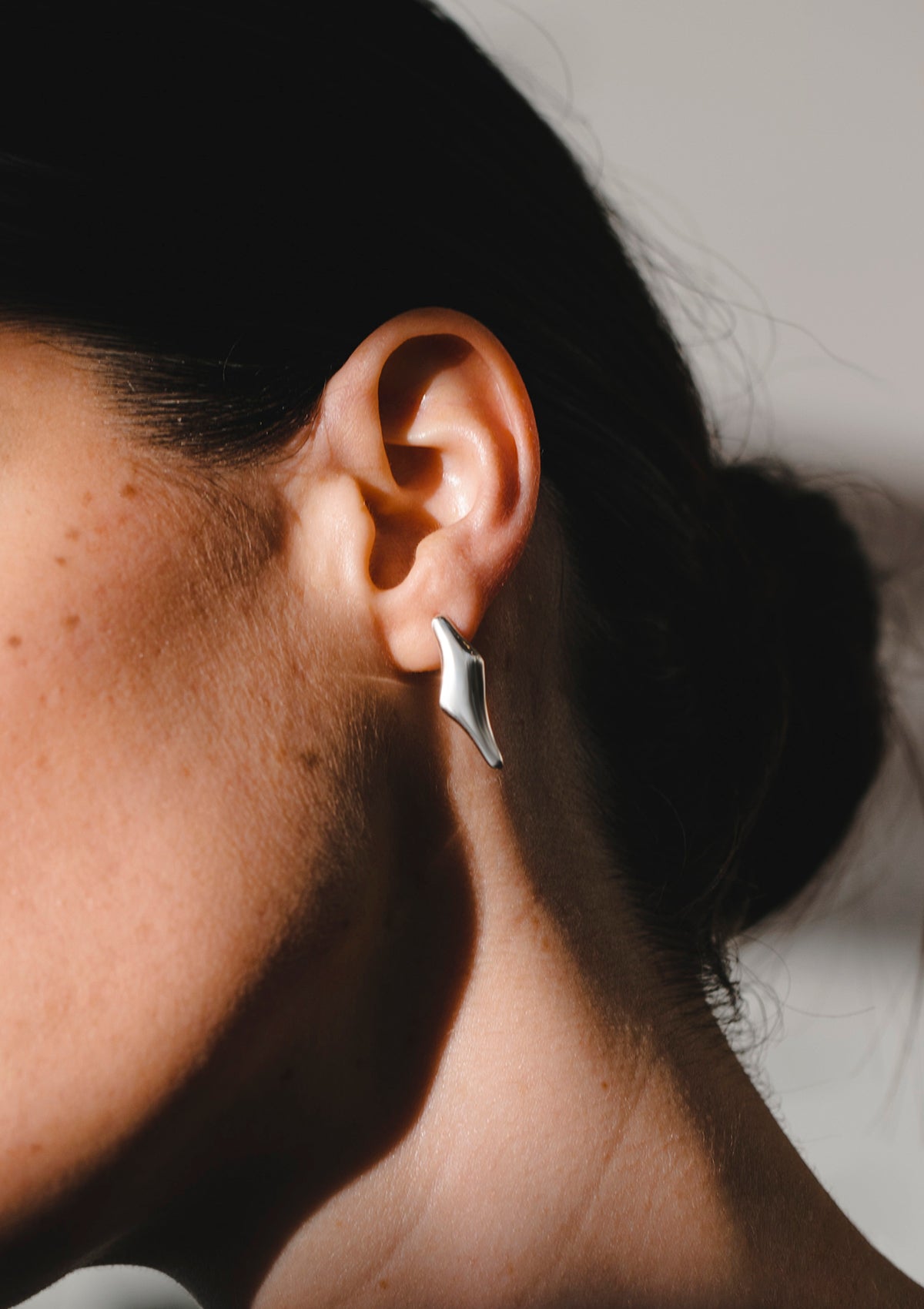 Flat-shaped sterling silver earrings worn close to ear, sculptural and medium in size