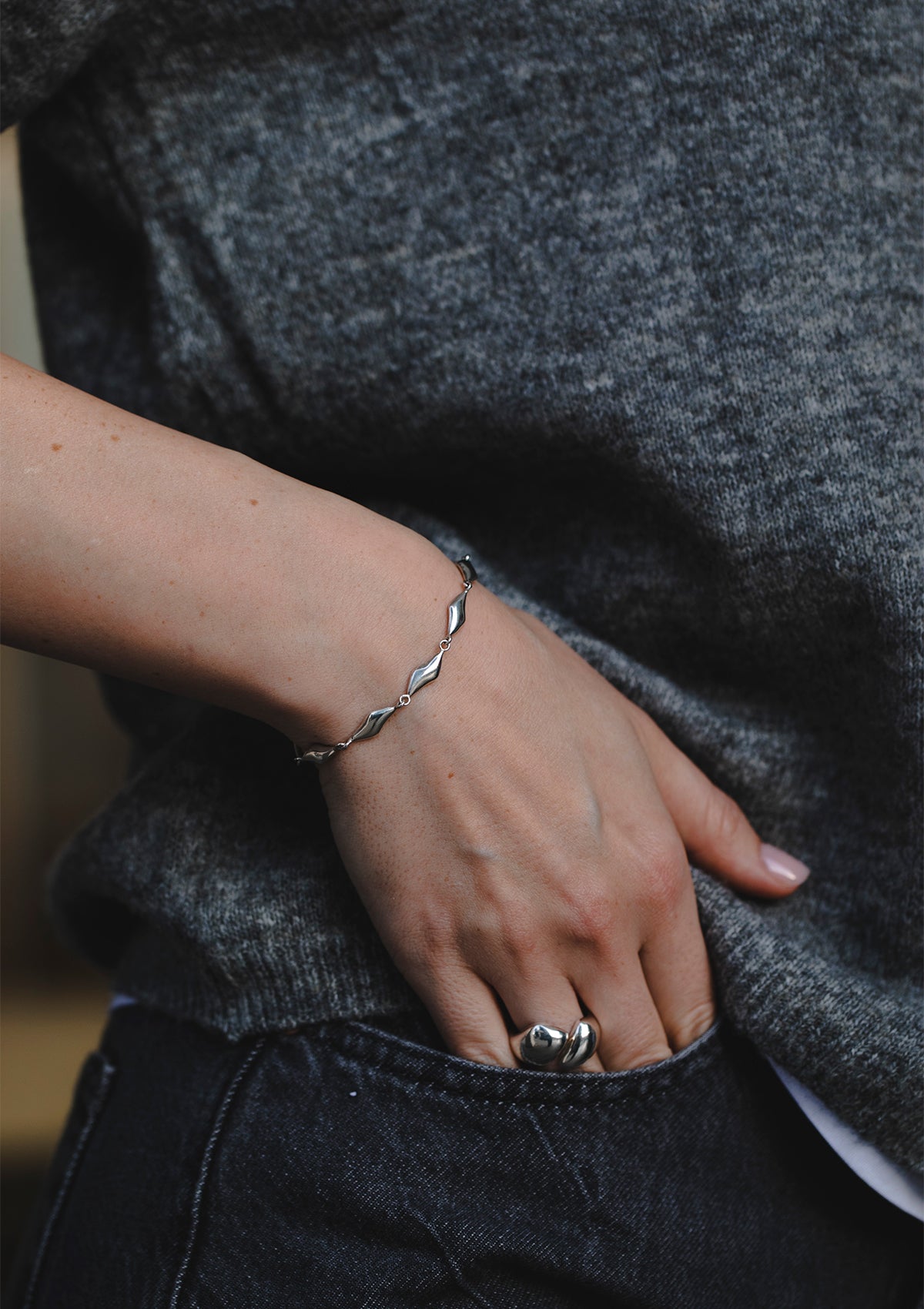 Elegant sterling silver bracelet with wavy waterform design, styled casually with knit top