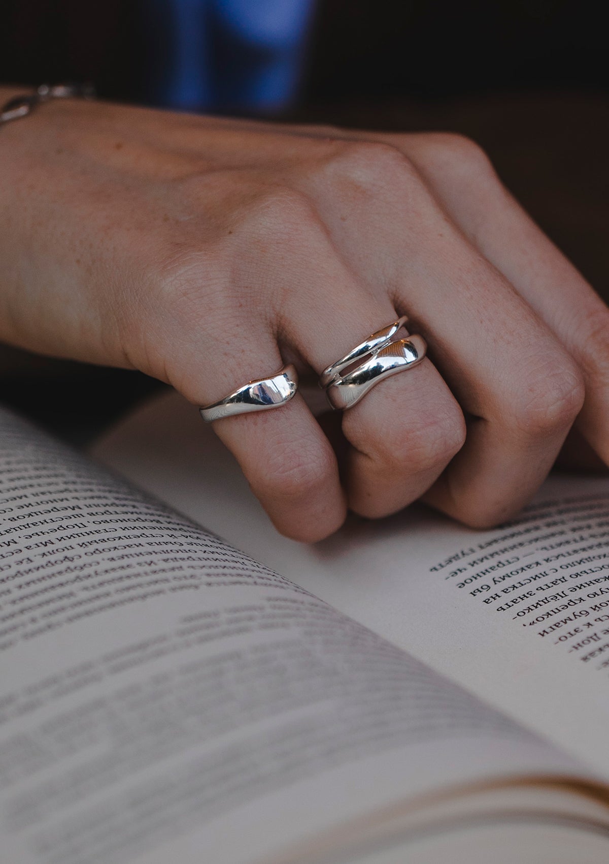 Sterling silver double band ring on hand holding open book – everyday wavy ring with reflective shine
