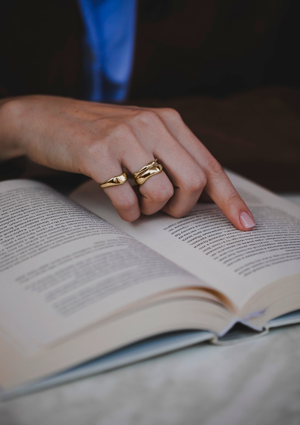 Model wearing sculptural 14k gold double ring while reading