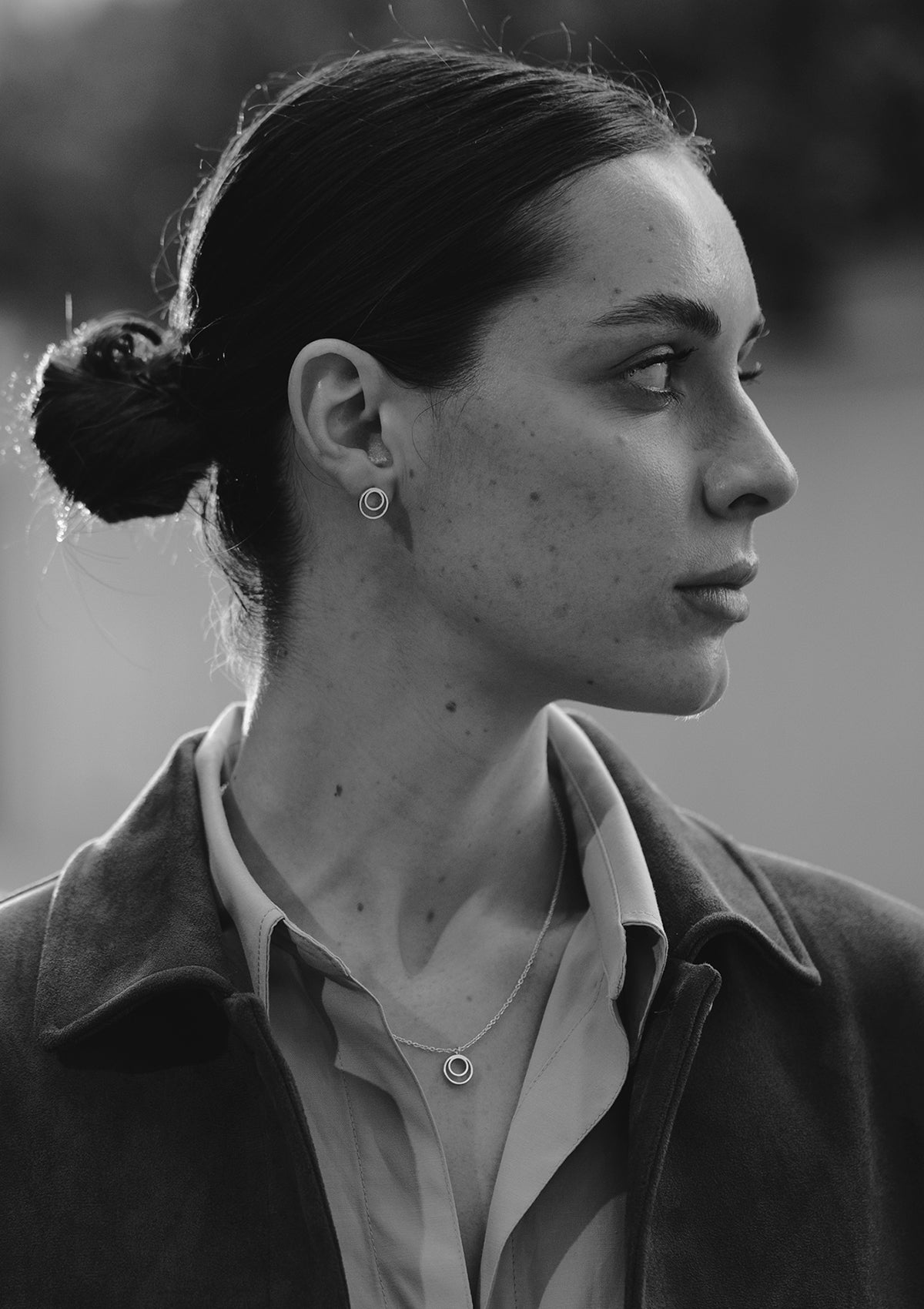 Elegant silver stud earrings with concentric circles, worn by model in sleek bun and blazer, side view