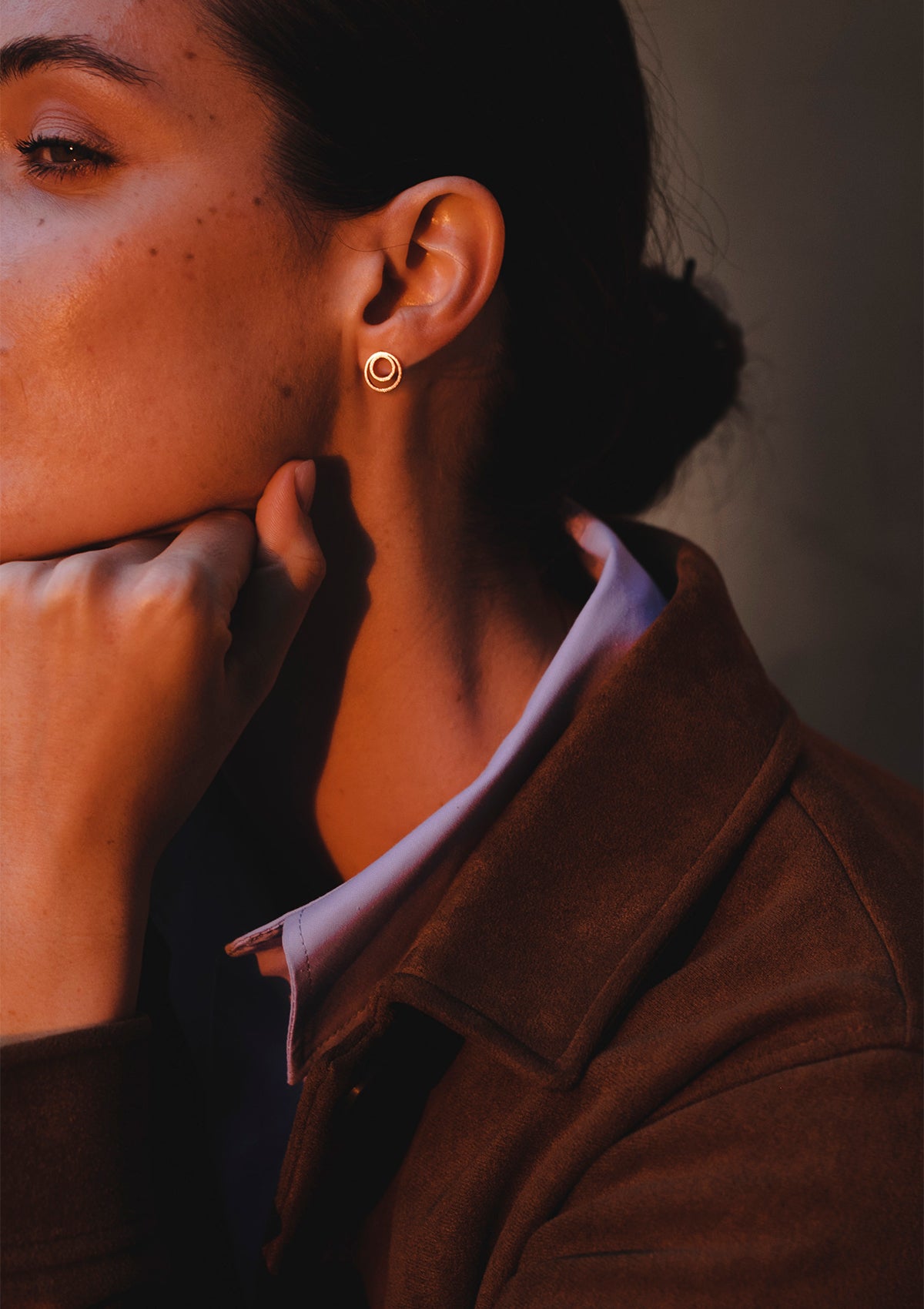 Concentric silver circle earrings styled casually, model resting hand on face, cozy and confident mood