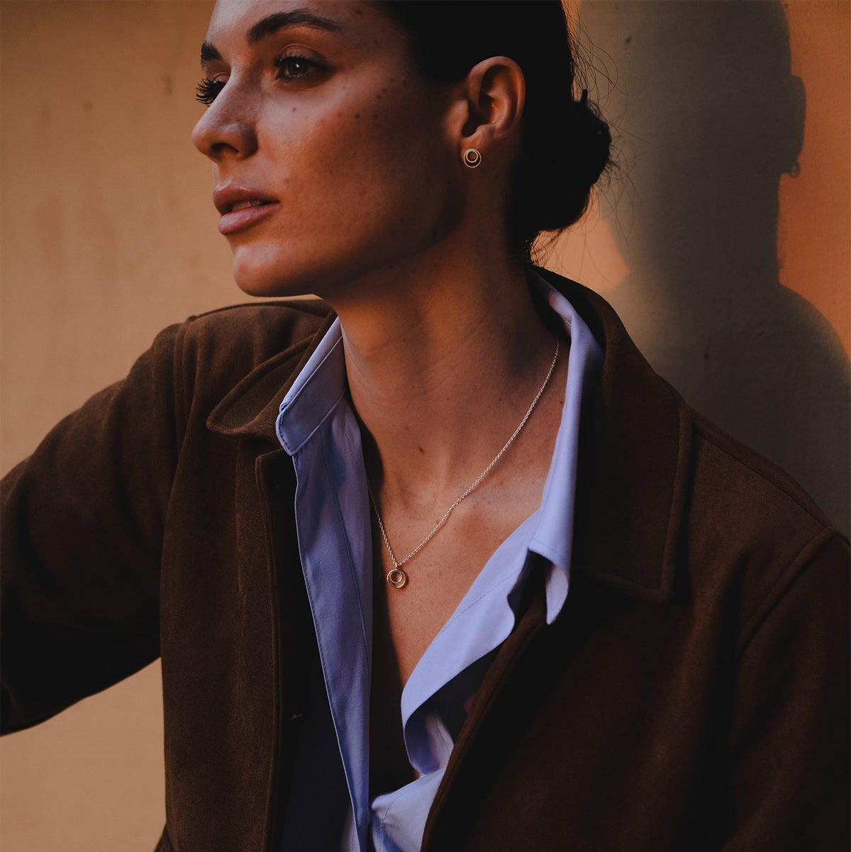 Silver double-circle stud earrings on model, warm lighting with natural makeup and earth-tone blouse