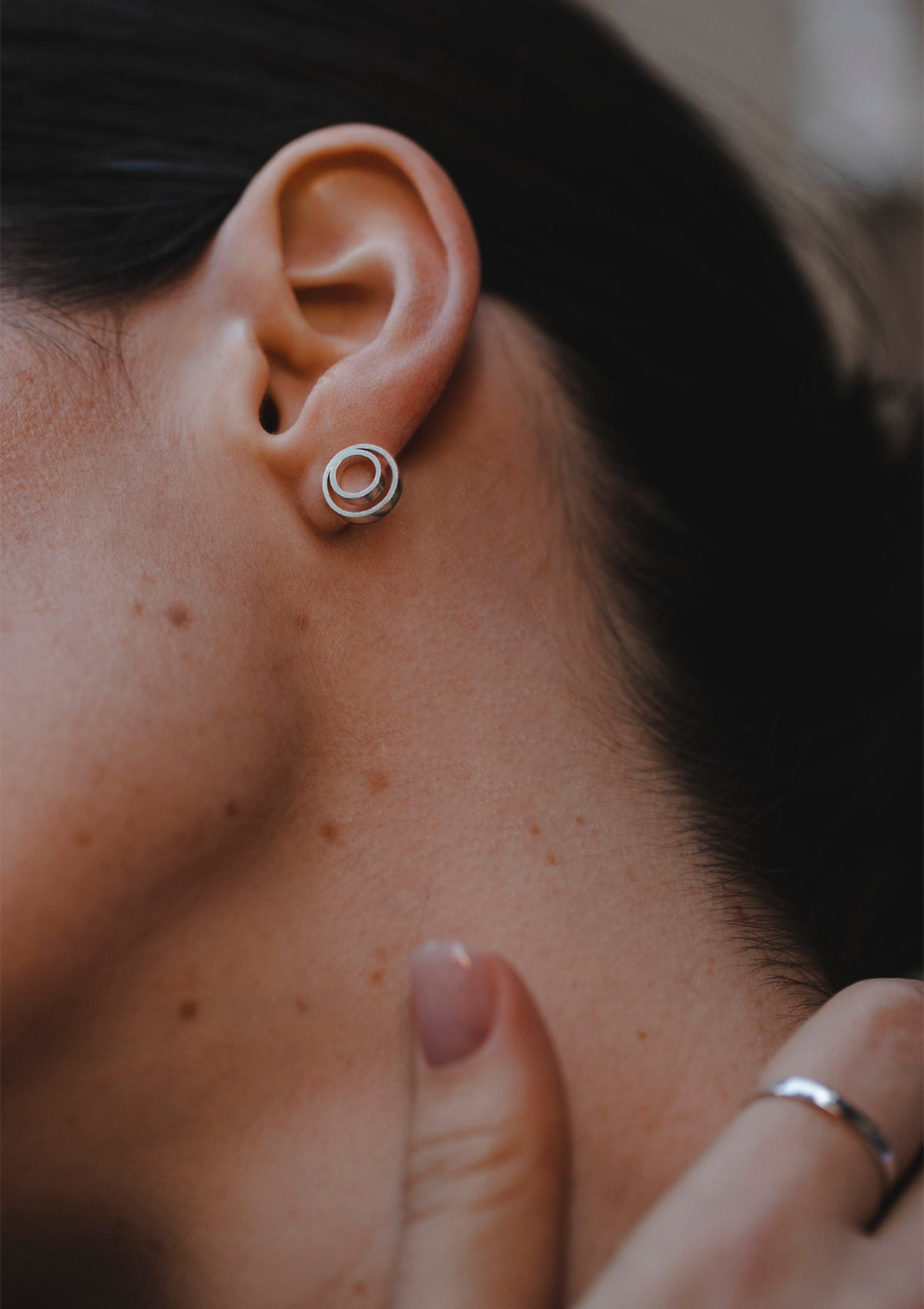 Minimalist geometric stud earring in sterling silver, detailed ear close-up with hand gesture, refined styling