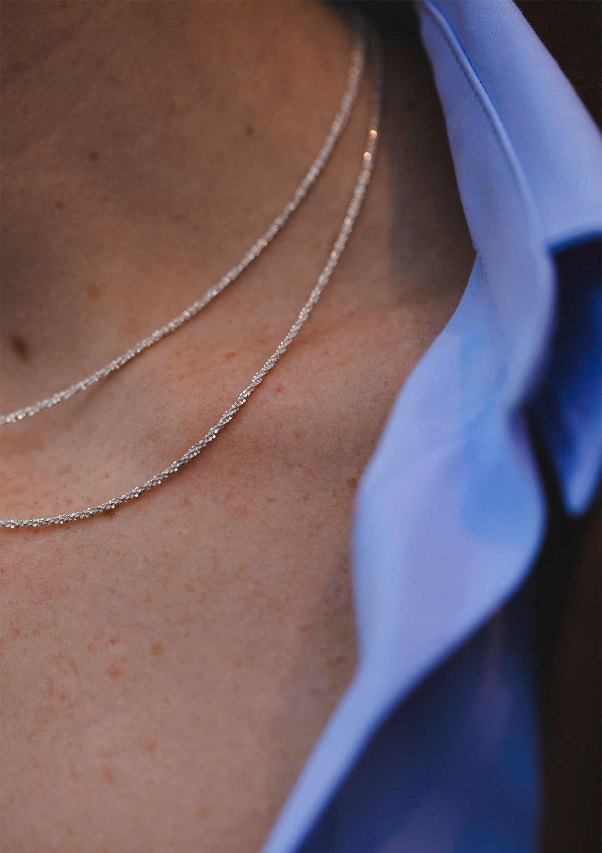 Minimalist silver choker necklace layered under open collar, focus on delicate sparkle and texture