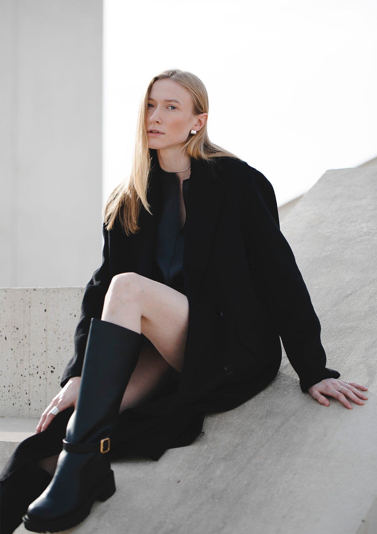 Silver wide hoops worn with all-black outfit, model seated on white steps, editorial styling with bold earring statement
