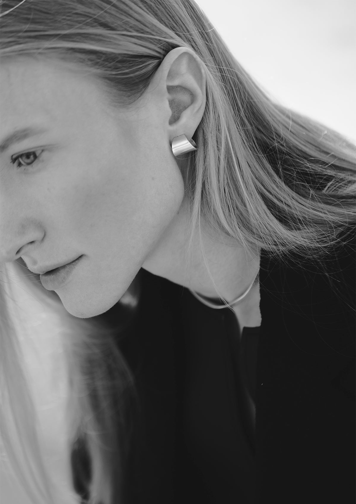 Soft black-and-white portrait showing brushed matte silver hoops, minimalist mood with model in motion