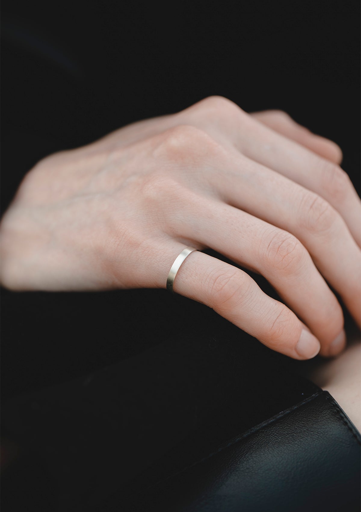 Close-up of hand resting on black fabric, showing 2 mm matte silver ring with subtle brushed texture and clean edge.