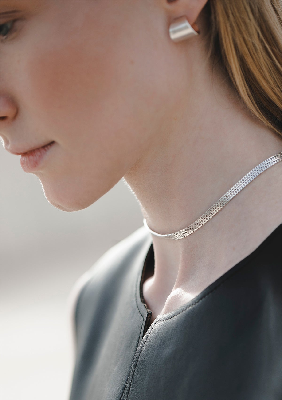 Delicate box chain choker in sterling silver, shimmering softly against model's skin, close-up profile shot