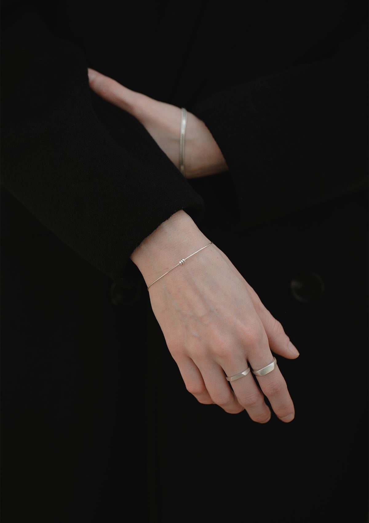 Delicate silver bracelet with three beads worn on wrist, arm crossing body in black clothing for contrast