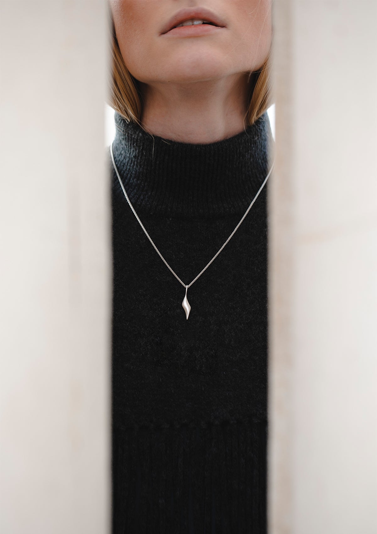 Long silver necklace with geometric drop charm, contemporary designer jewelry styled casually