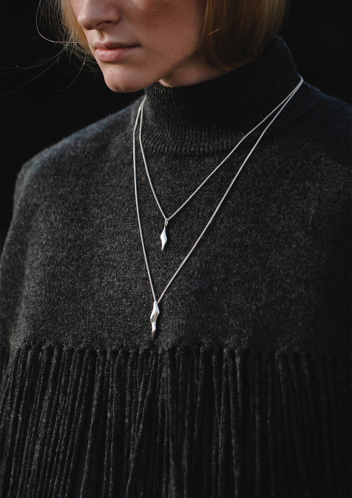 Statement silver necklace with bold wavy pendant on long chain, worn over black top