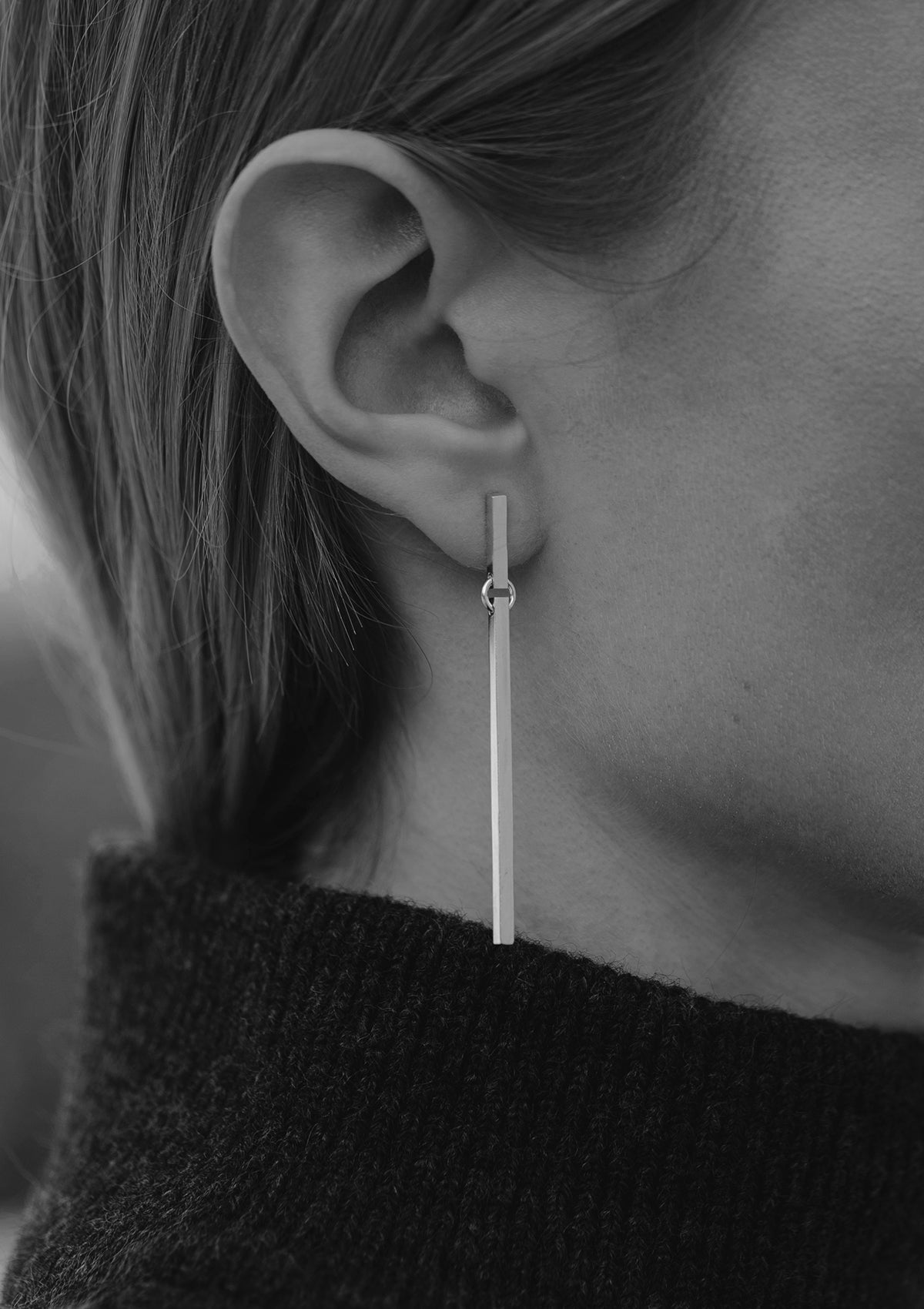 Monochrome close-up of long silver earrings in square profile, minimalist style captured on model’s ear