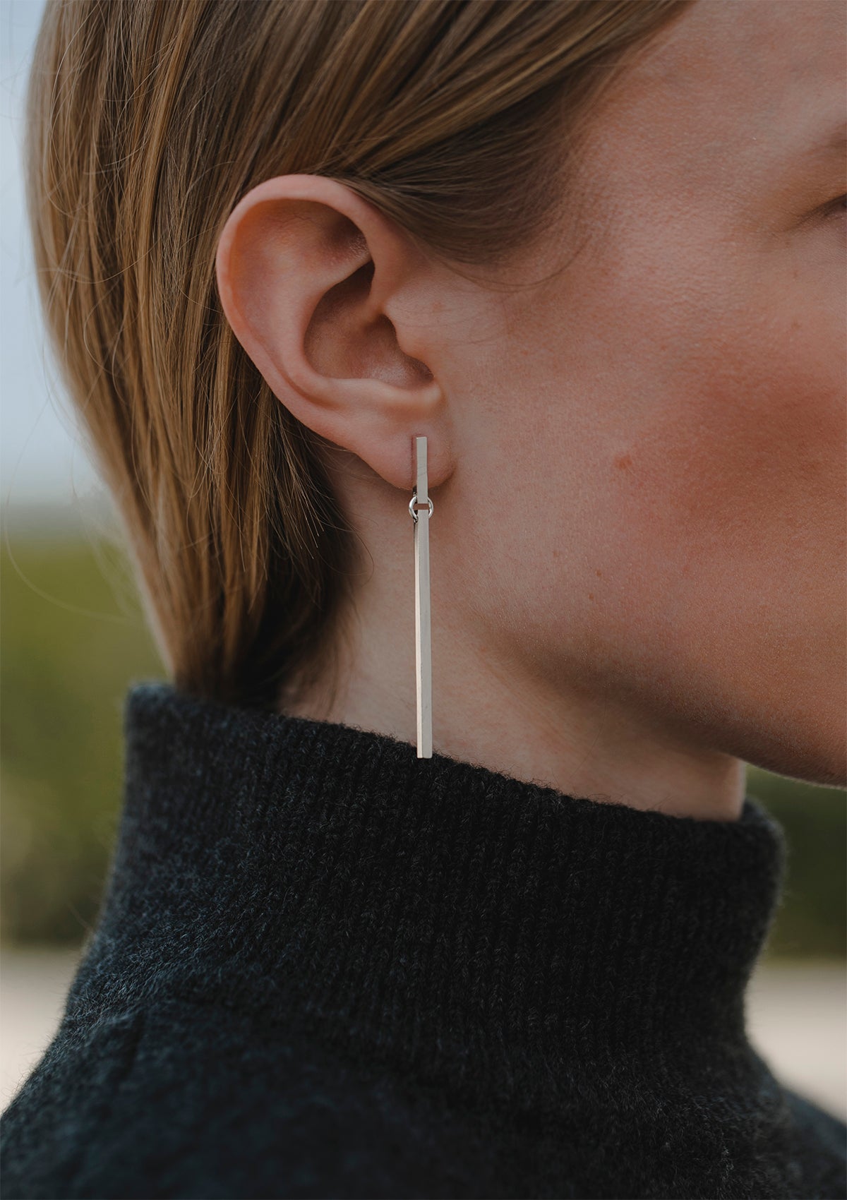 Long silver stud earrings with square wire drop, worn by model with hair tucked behind ear, modern and lightweight look