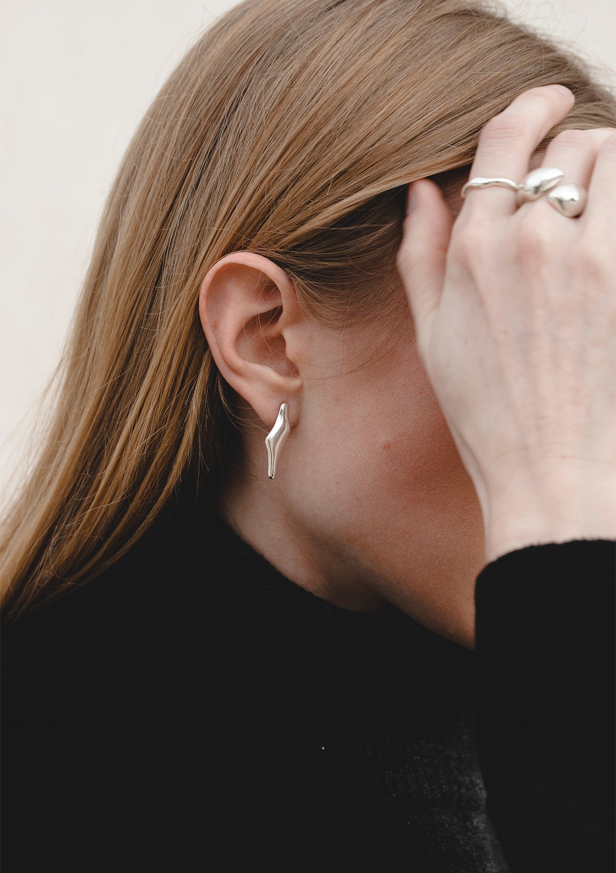 Sculptural silver ring worn on hand, minimalist statement jewelry styled with blonde hair