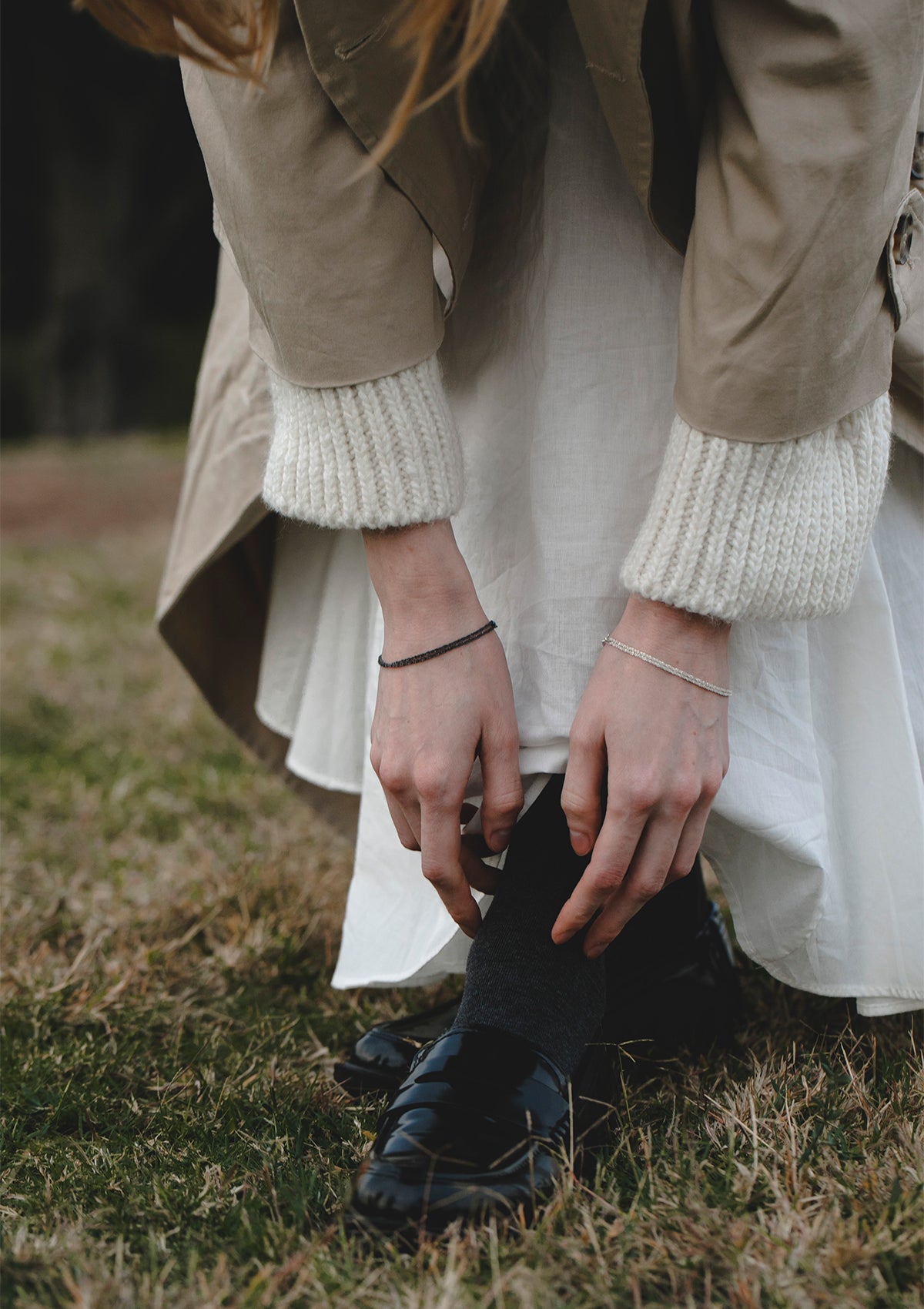 Casual styling of double silver bracelet worn with white knitwear, lifestyle moment outdoors with minimalist jewelry accent
