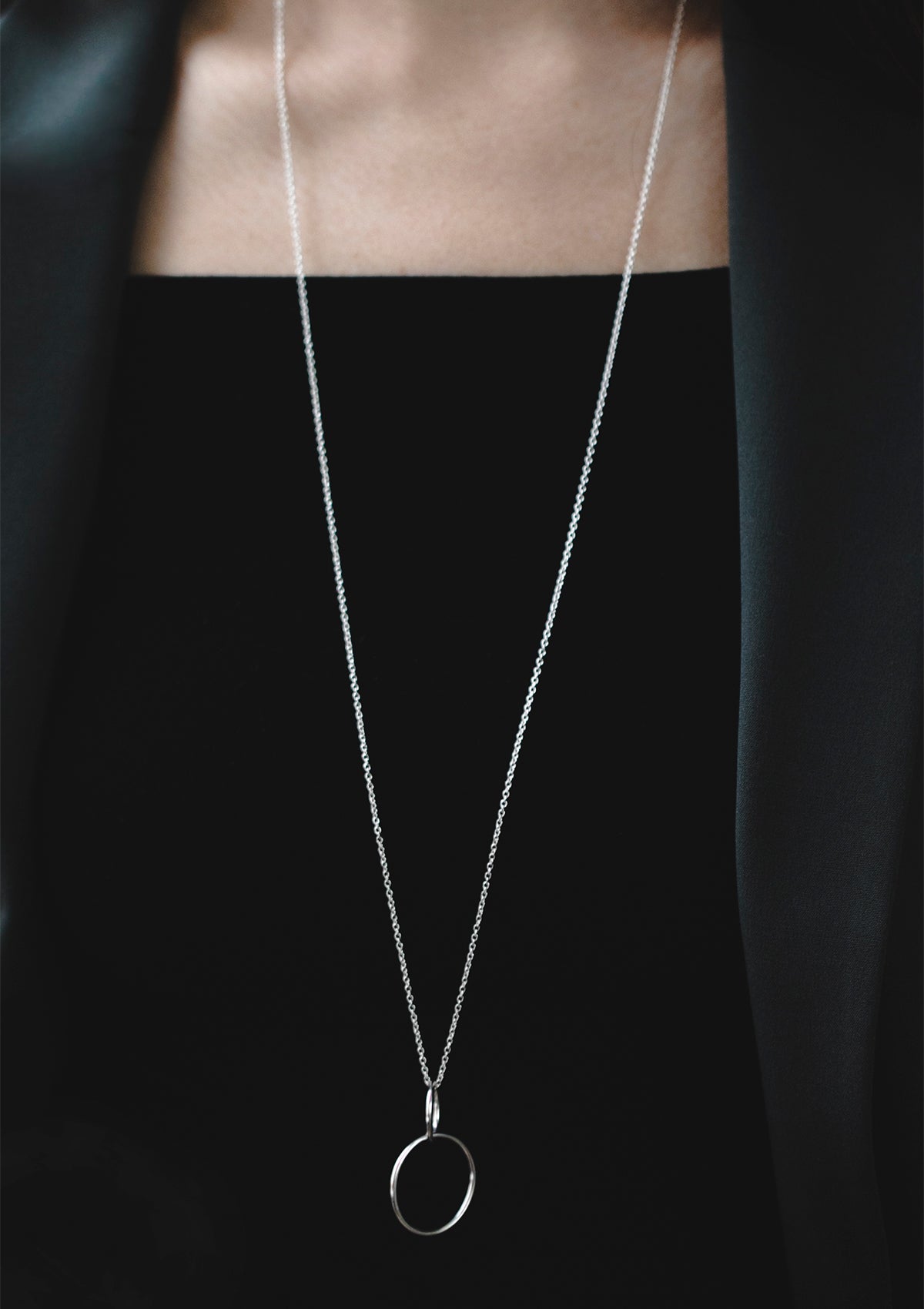 Long silver chain necklace with double circle pendant worn over black top, sleek and elegant look