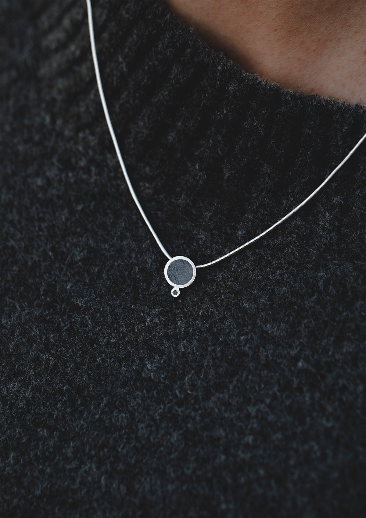Concrete pendant necklace with silver frame worn over dark knit, modern architectural accent