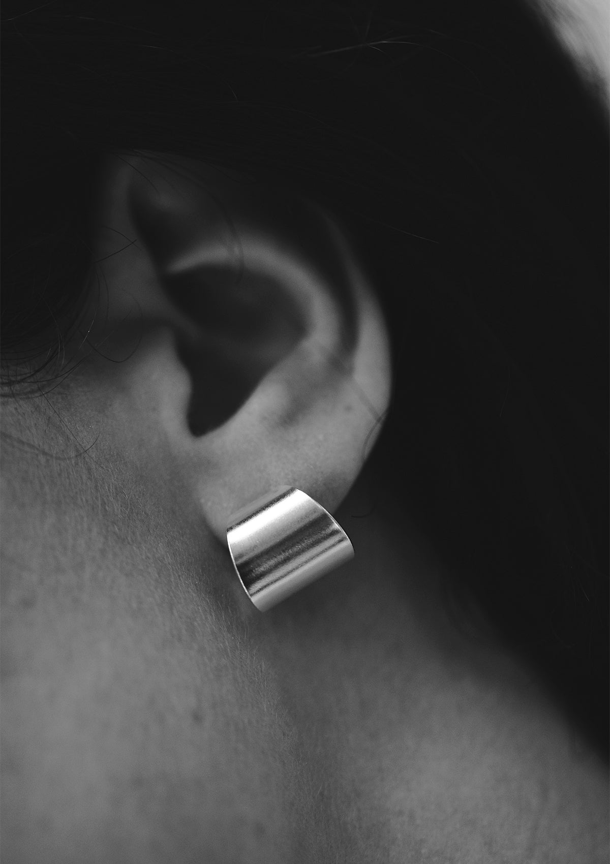 Detail shot of geometric silver hoop on ear, square-profile curves highlighted in shadow, clean and minimal aesthetic