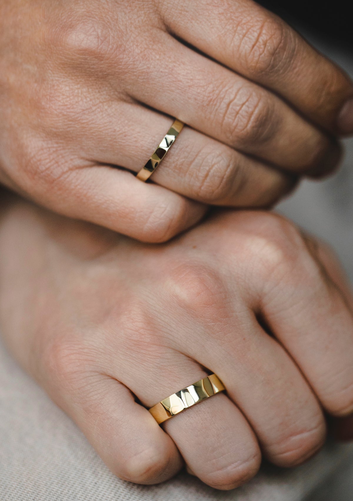 Man and woman wearing matching faceted shiny gold rings with soft-edged hammered texture – minimalist wedding bands
