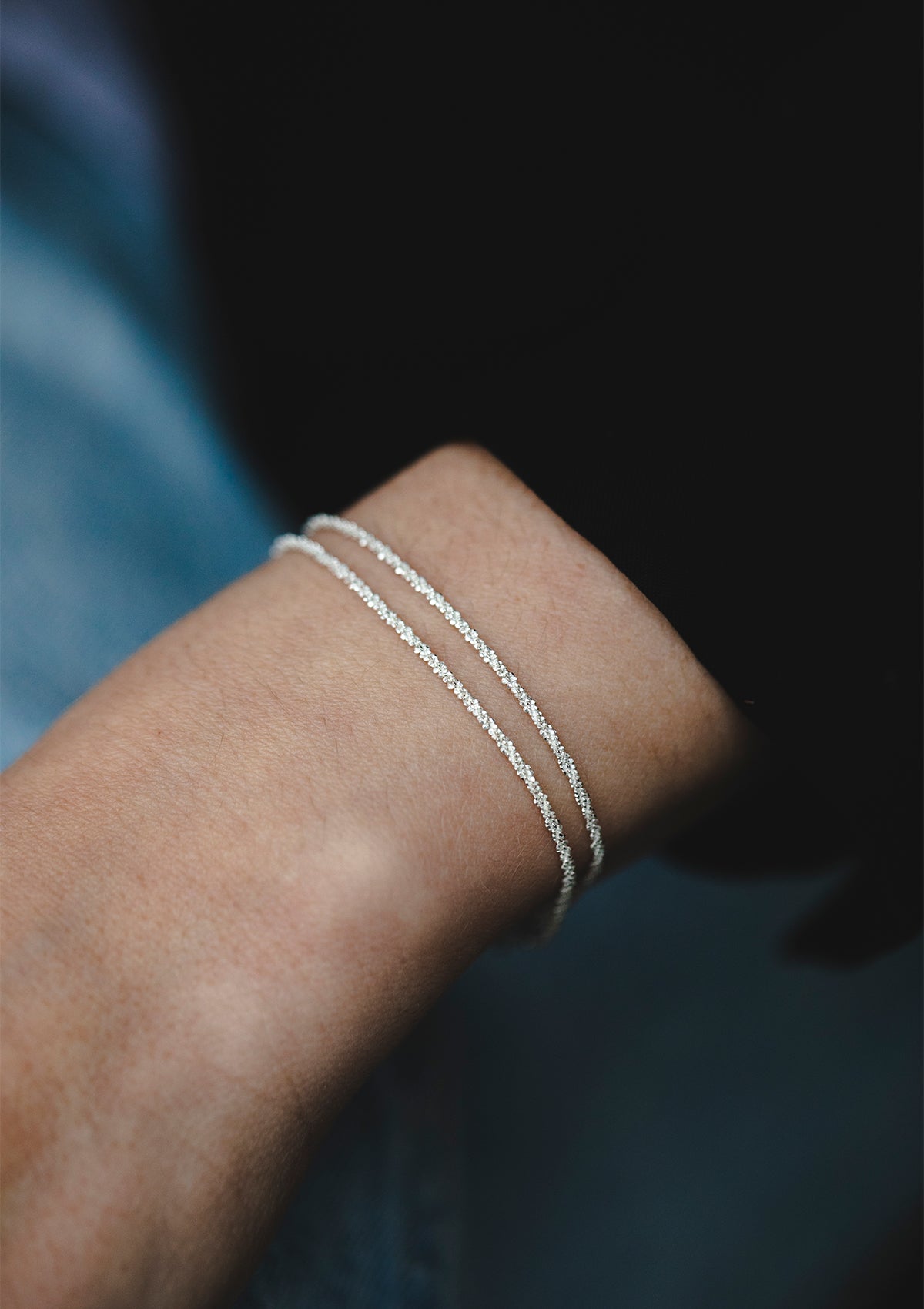 Sterling silver double chain bracelet, shimmering in soft light, shown on wrist in elegant close-up