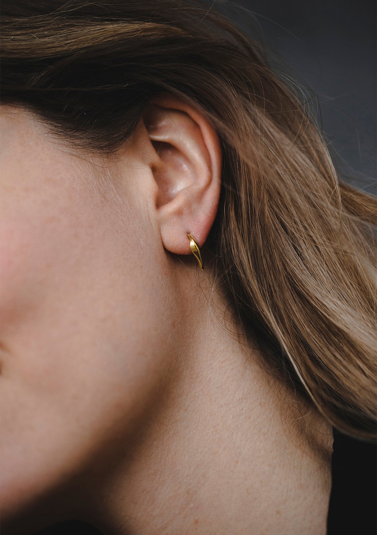 Tiny gold stud earrings with soft floral curve, elegant handcrafted design worn close to ear
