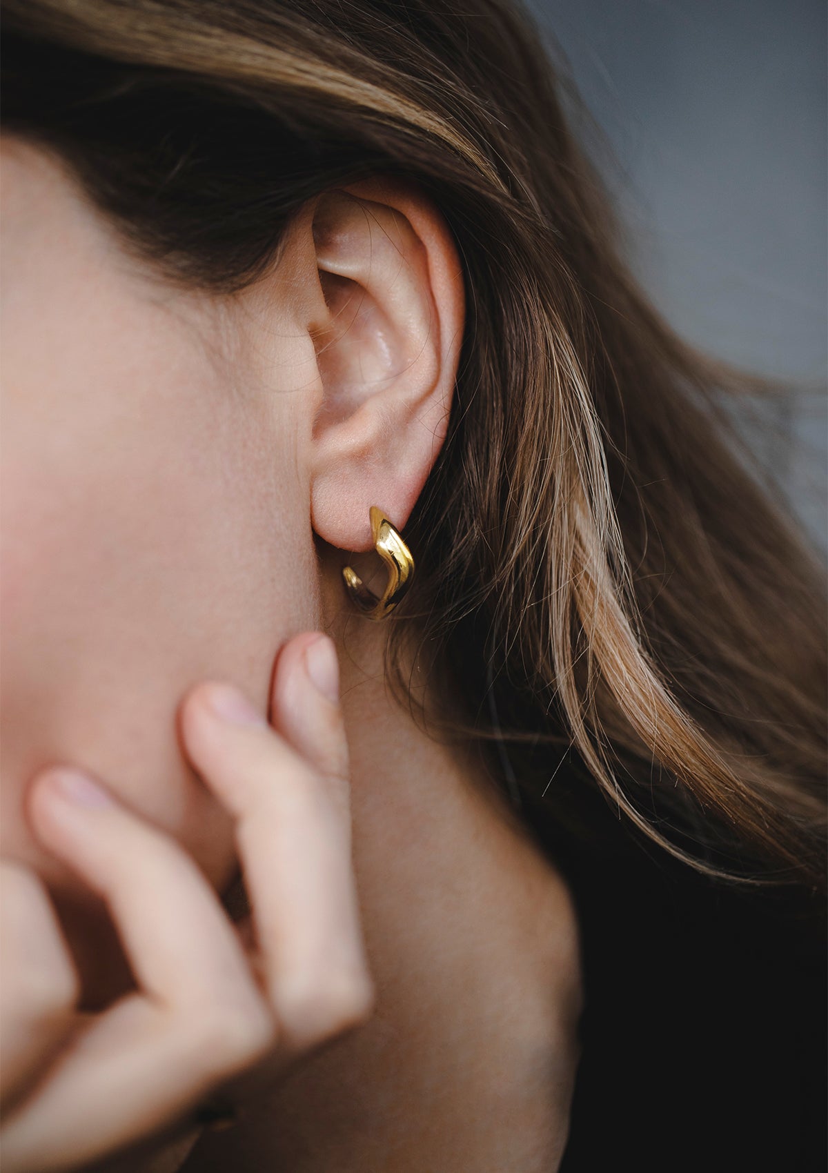 Real gold wavy hoop earrings worn in ear, elegant everyday jewelry in shiny finish