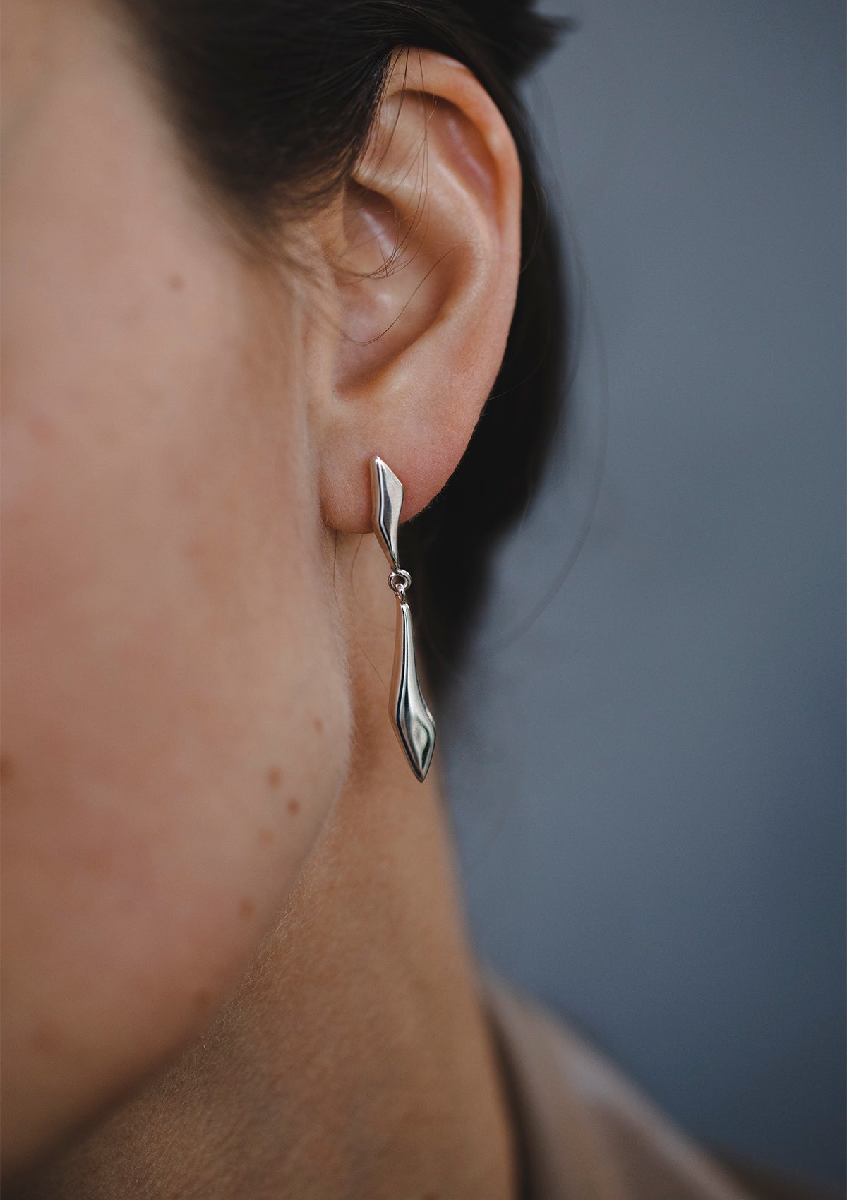 Statement silver dangle earring shown in ear, contemporary drop style with smooth shine