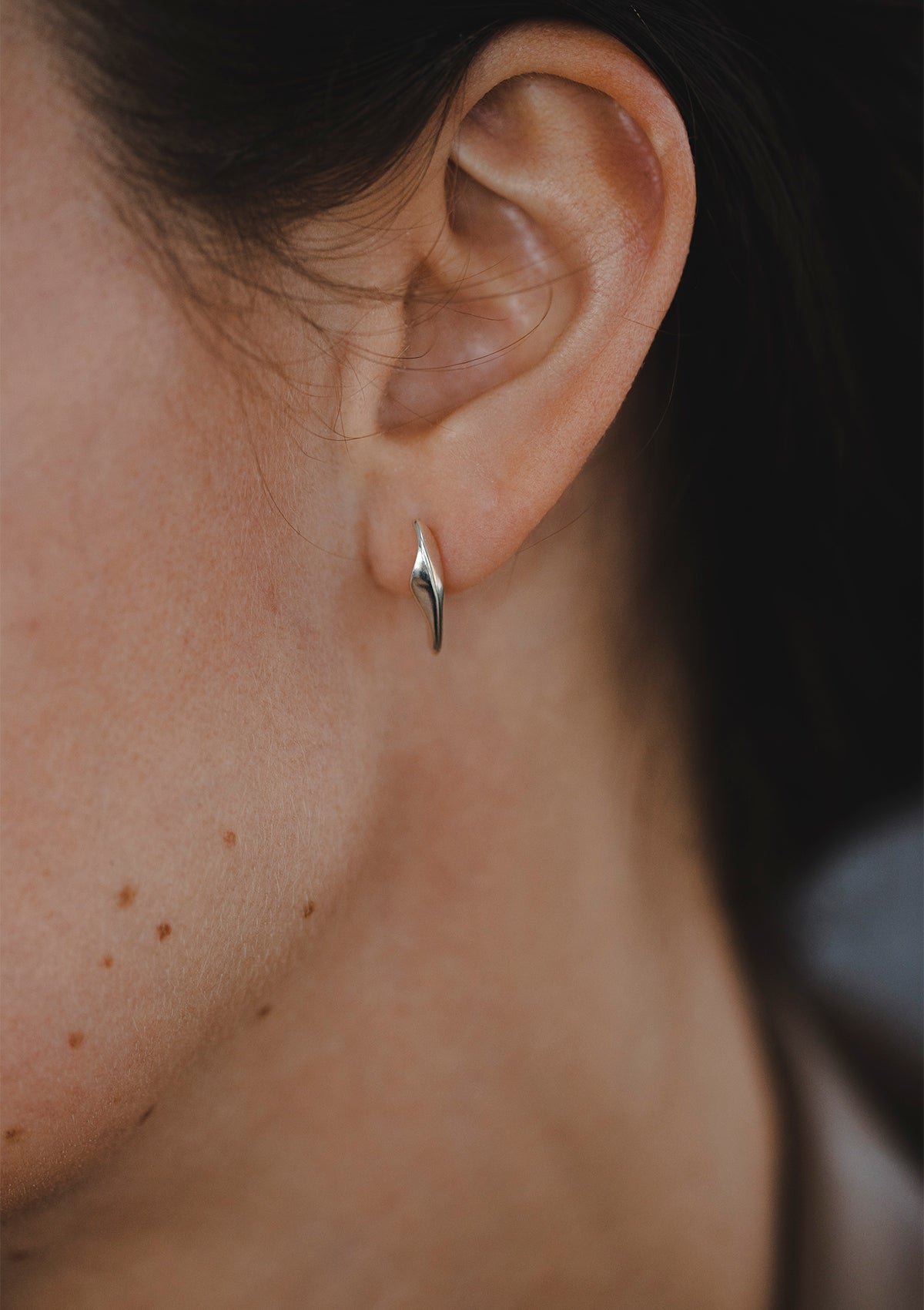 Tiny silver earrings worn close to the ear, delicate handcrafted design with subtle organic shape