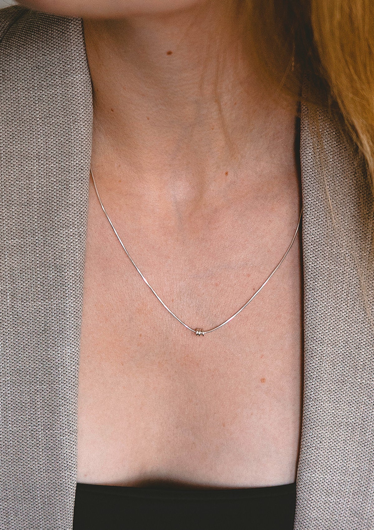 Three-ball silver necklace on model wearing natural-toned jacket, timeless minimal jewelry styling