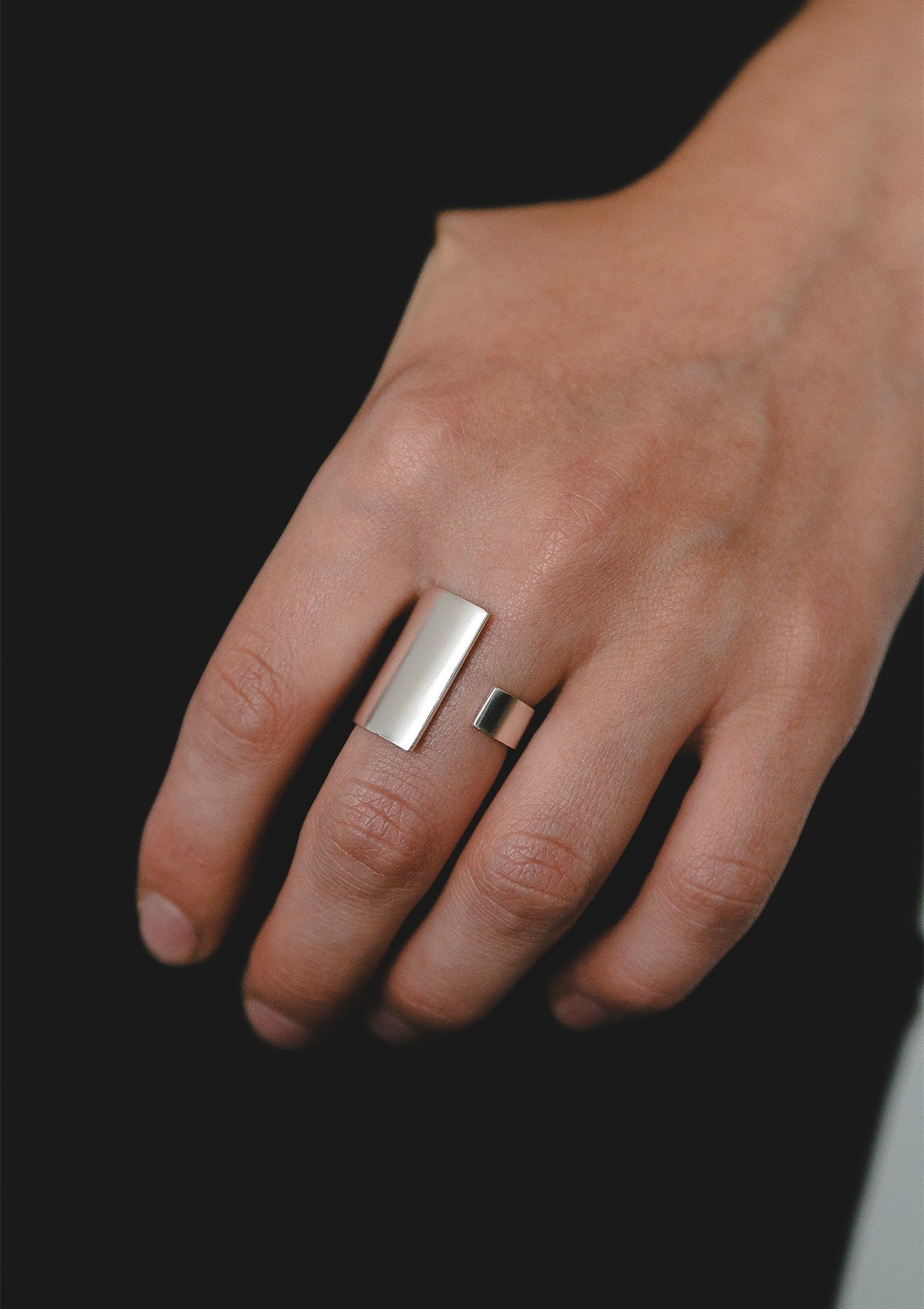 Sculptural sterling silver ring with architectural silhouette, semi-matte surface highlighted by directional light on dark