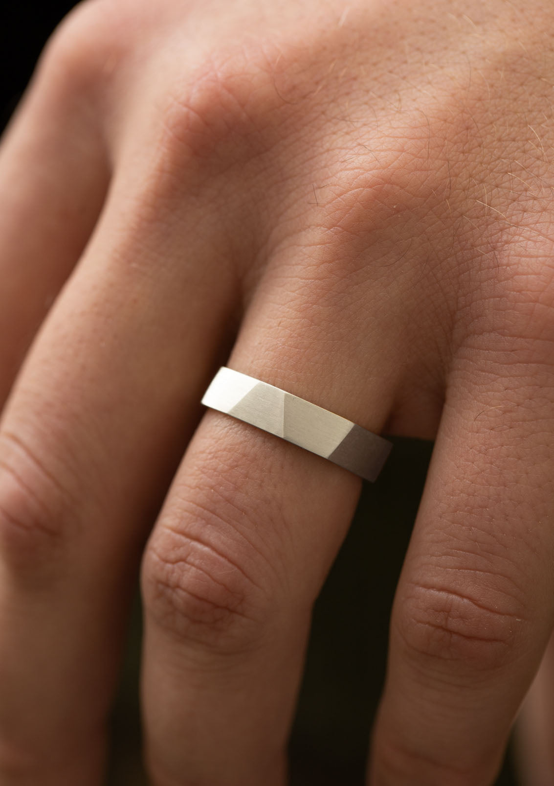 Minimalist sterling silver ring with faceted matte finish worn on man’s finger – modern men’s design