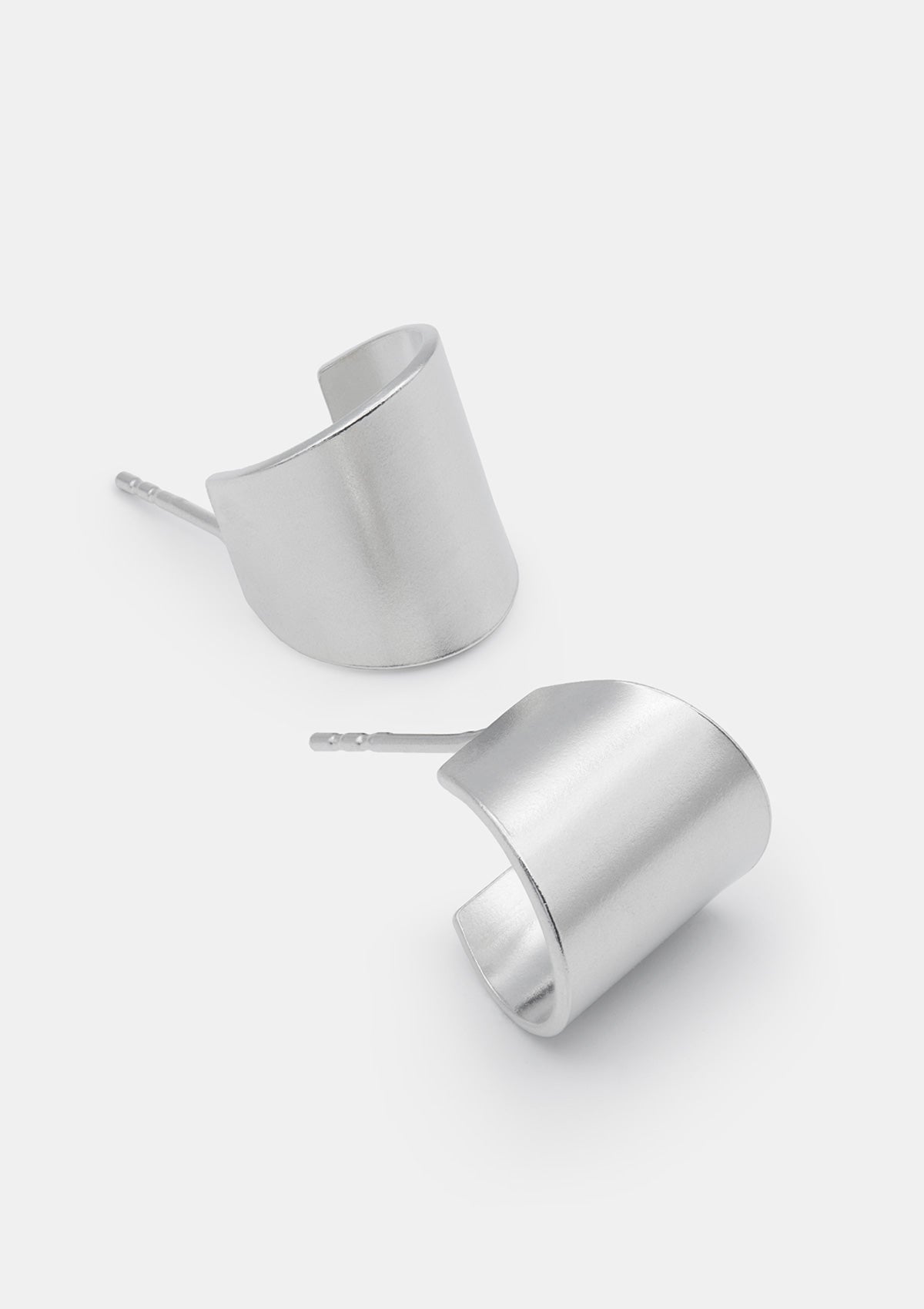 Wide geometric hoop earrings in sterling silver, minimal sculptural shape, displayed on clean white background