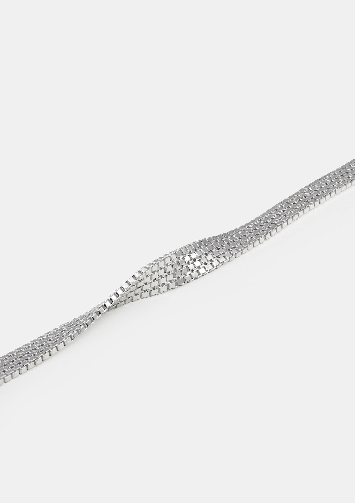 Sterling silver flat chain bracelet with soft reflection, shown coiled on neutral white textile surface, product texture focus