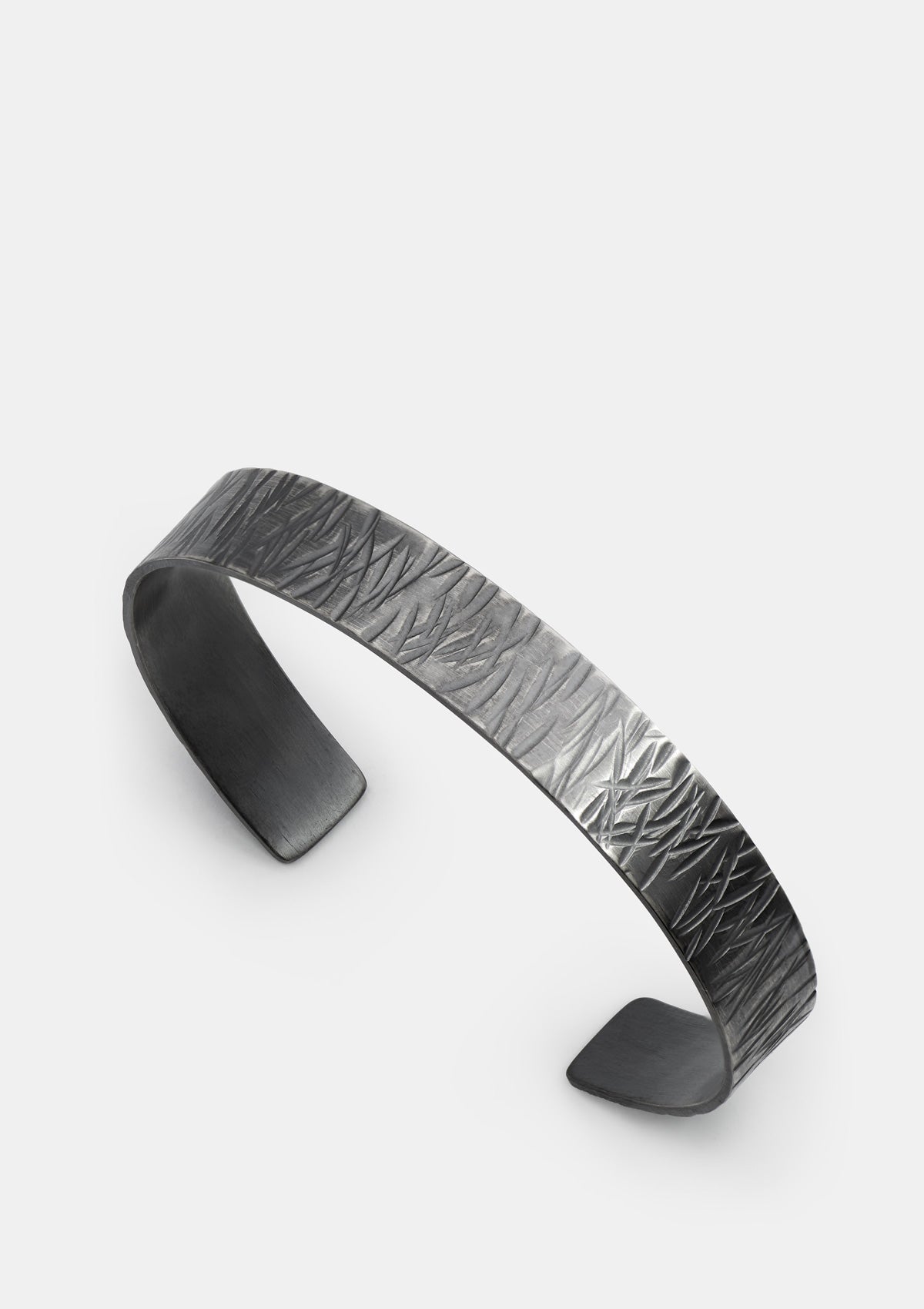 Oxidized sterling silver cuff bracelet, wide hammered texture, laid flat on light gray surface