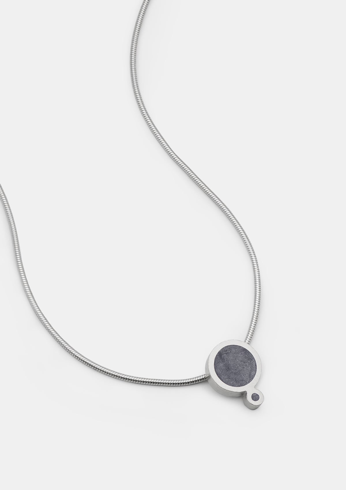 Minimalist silver necklace with geometric double-circle pendant, filled with dark gray concrete mix, laid on white background