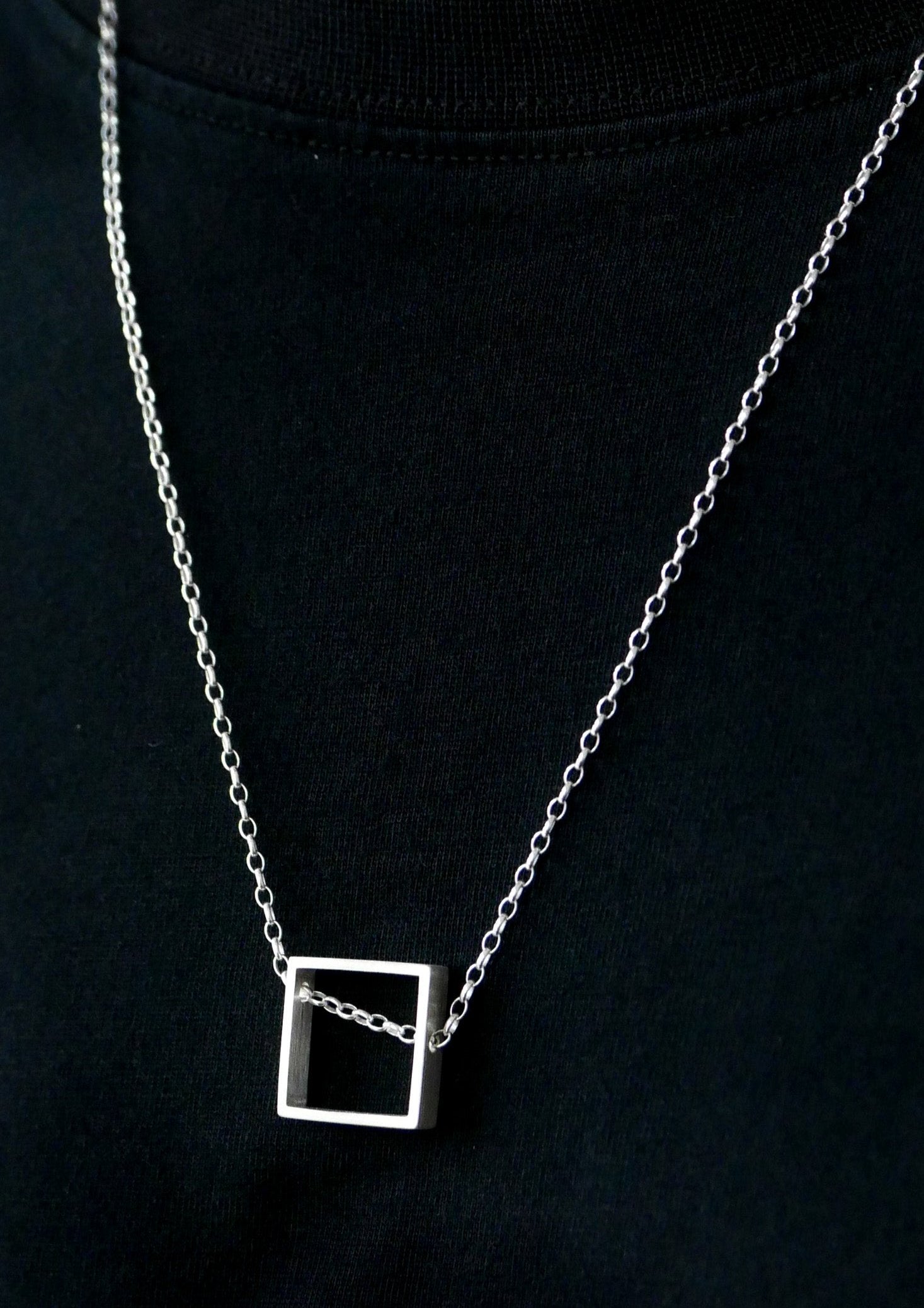 Minimalist silver square pendant hanging off-center on model's chest, delicate chain over black fabric