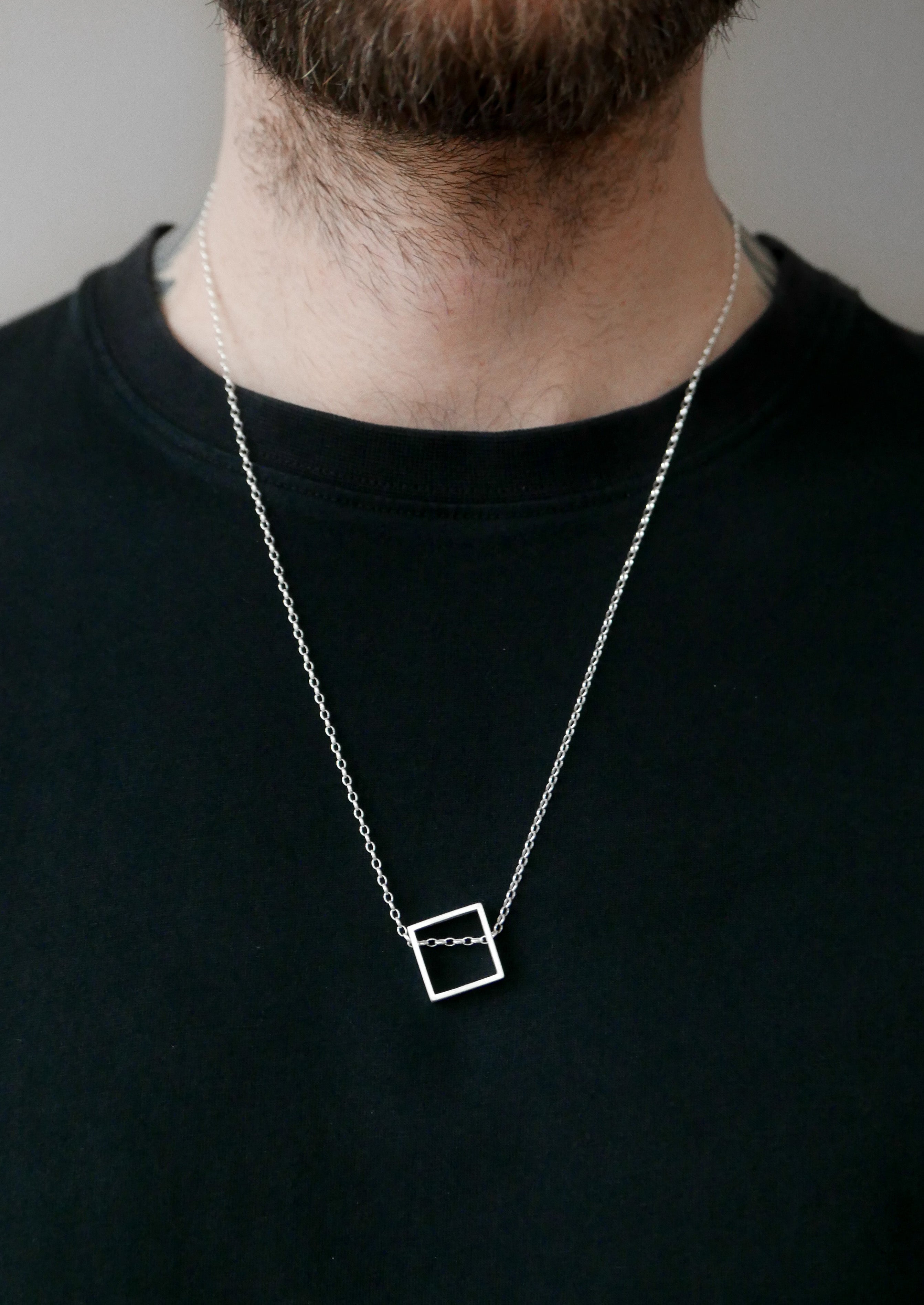 Small silver square pendant necklace resting just off-center on neckline, matte finish and minimal styling