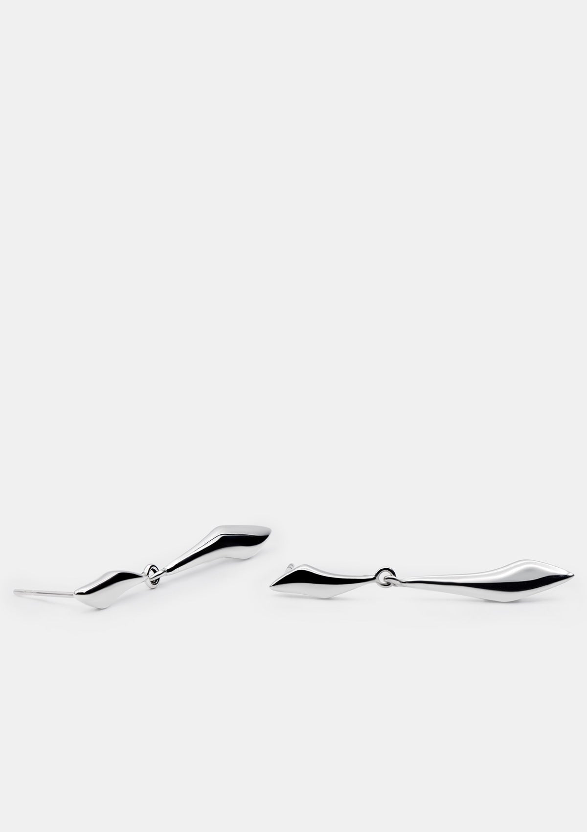 Sculptural sterling silver earrings photographed flat, sleek modern pendant drops