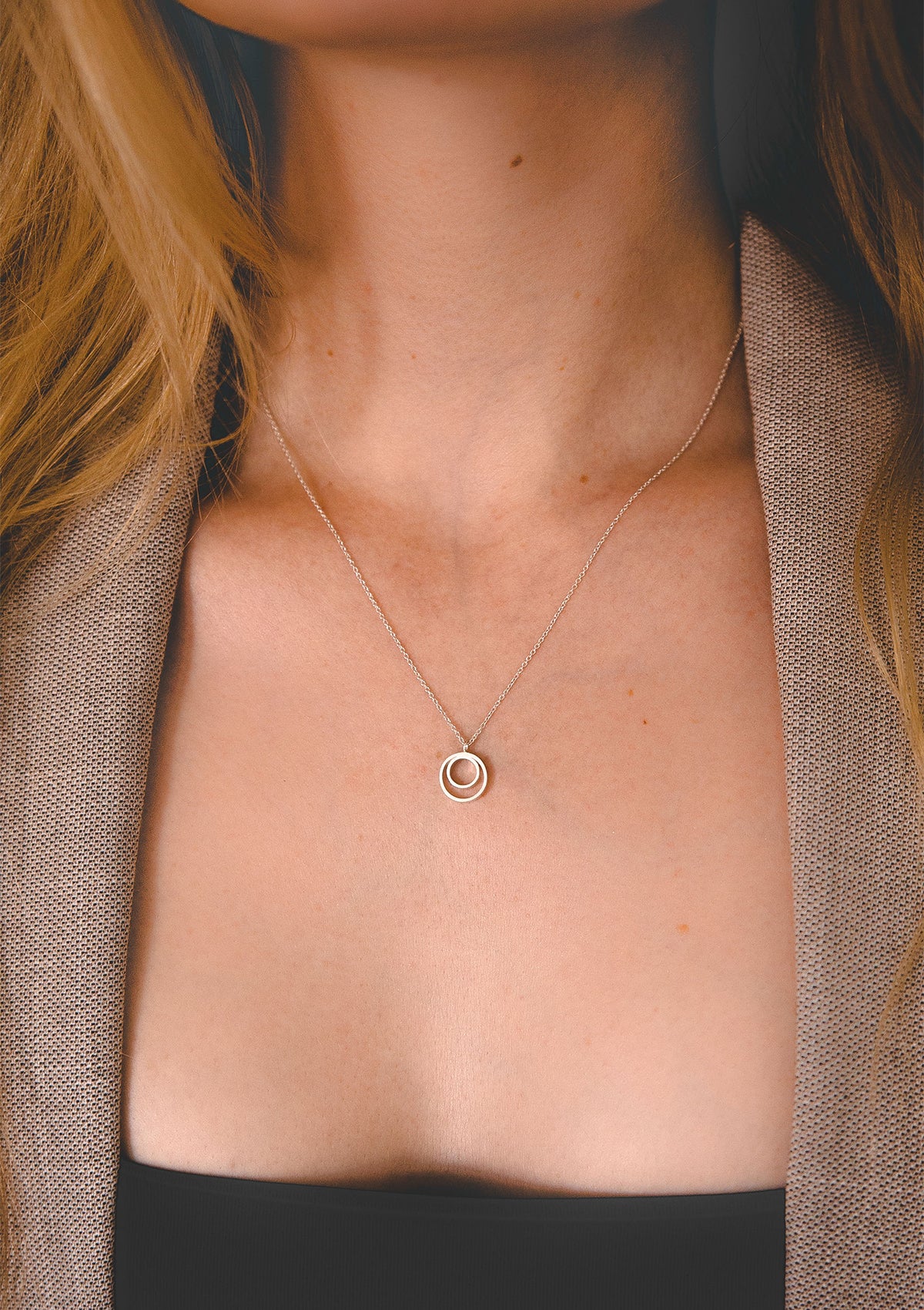 Delicate silver necklace with geometric circle pendant, styled with open beige blazer for elegant contrast