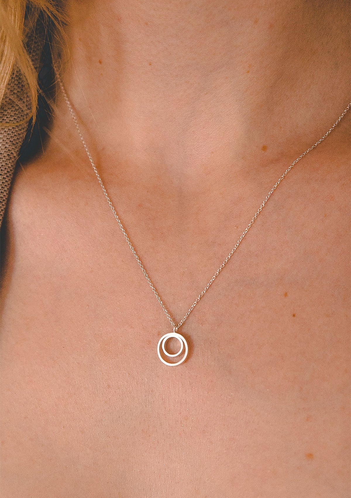 Minimalist silver pendant necklace, close view of concentric circles on model’s skin