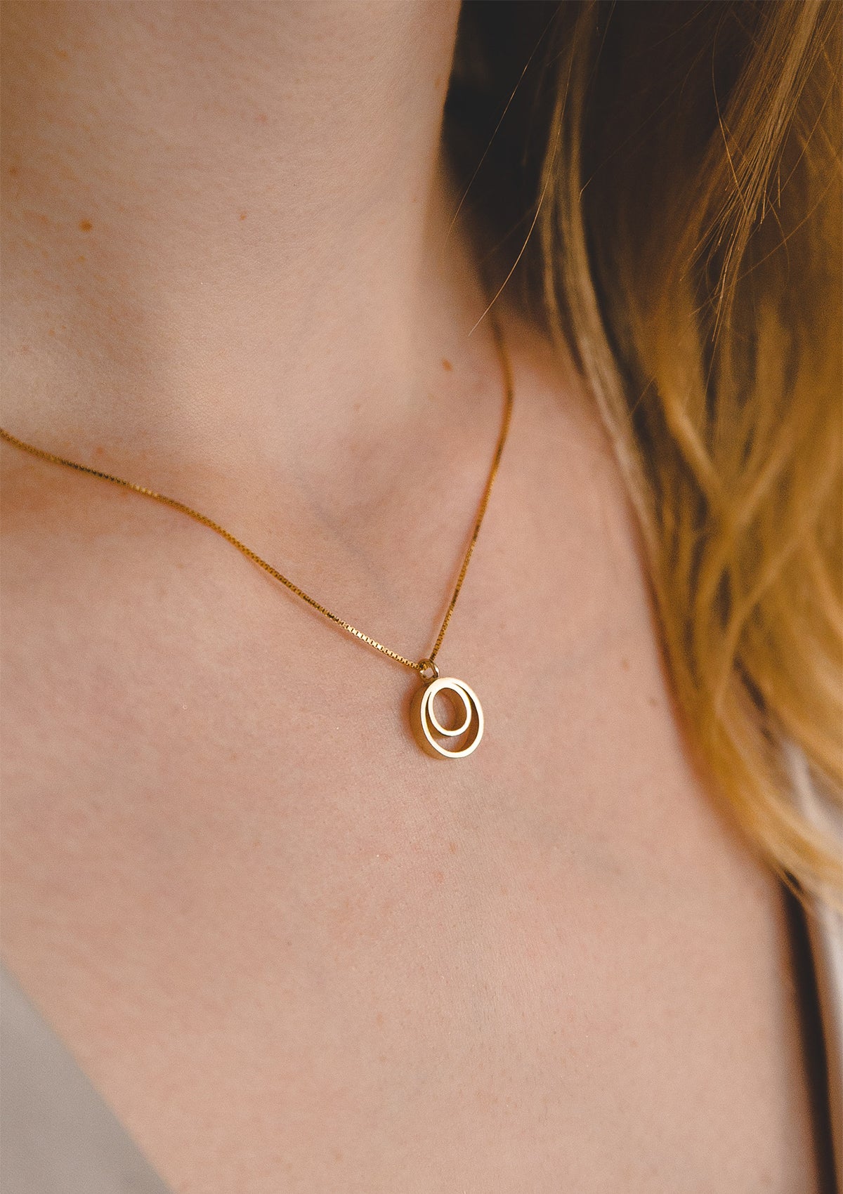 Delicate gold necklace with double circle pendant, minimalist 14K jewelry styled with natural soft lighting