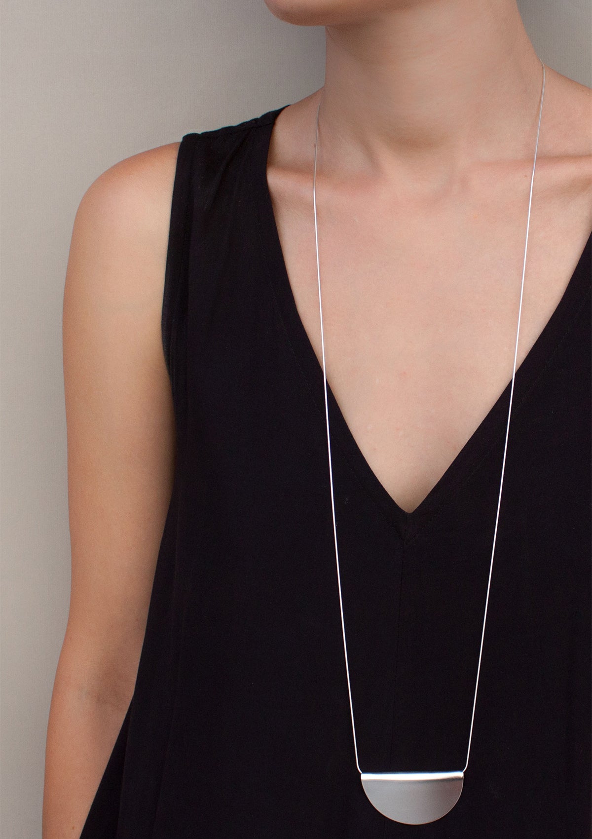 Minimalist silver necklace with oversized arc pendant, styled with sleeveless black top, highlighting simple bold silhouette