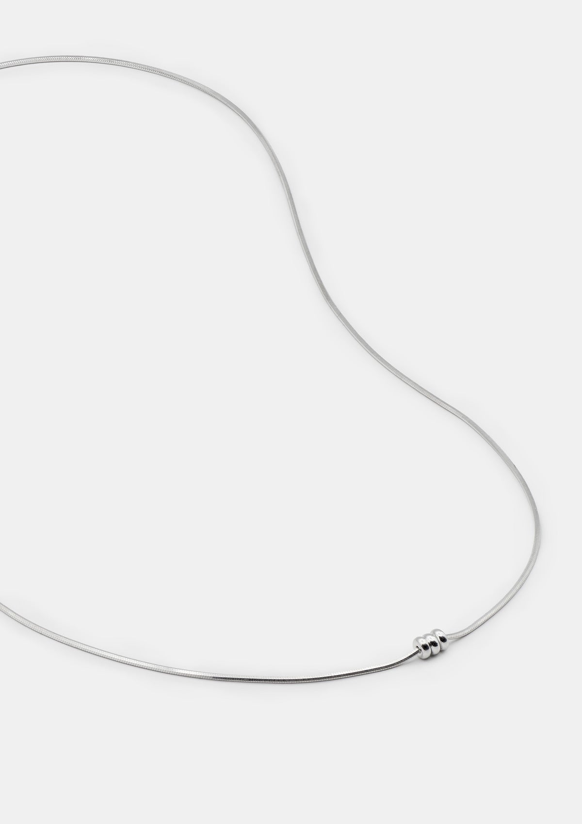Delicate silver necklace with three polished spheres, minimalist design, laid out on white background