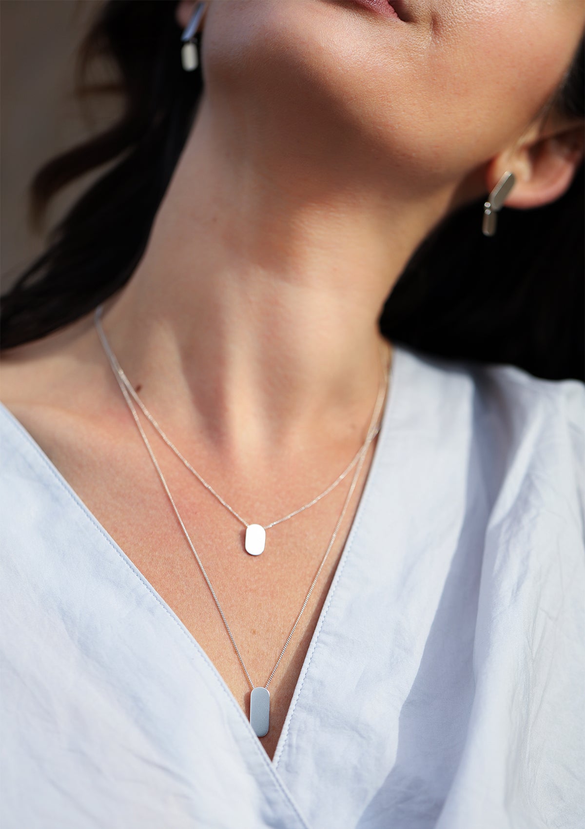 Minimalist silver necklace duo with oval pendants, sparkling matte texture, graceful layering from a side angle