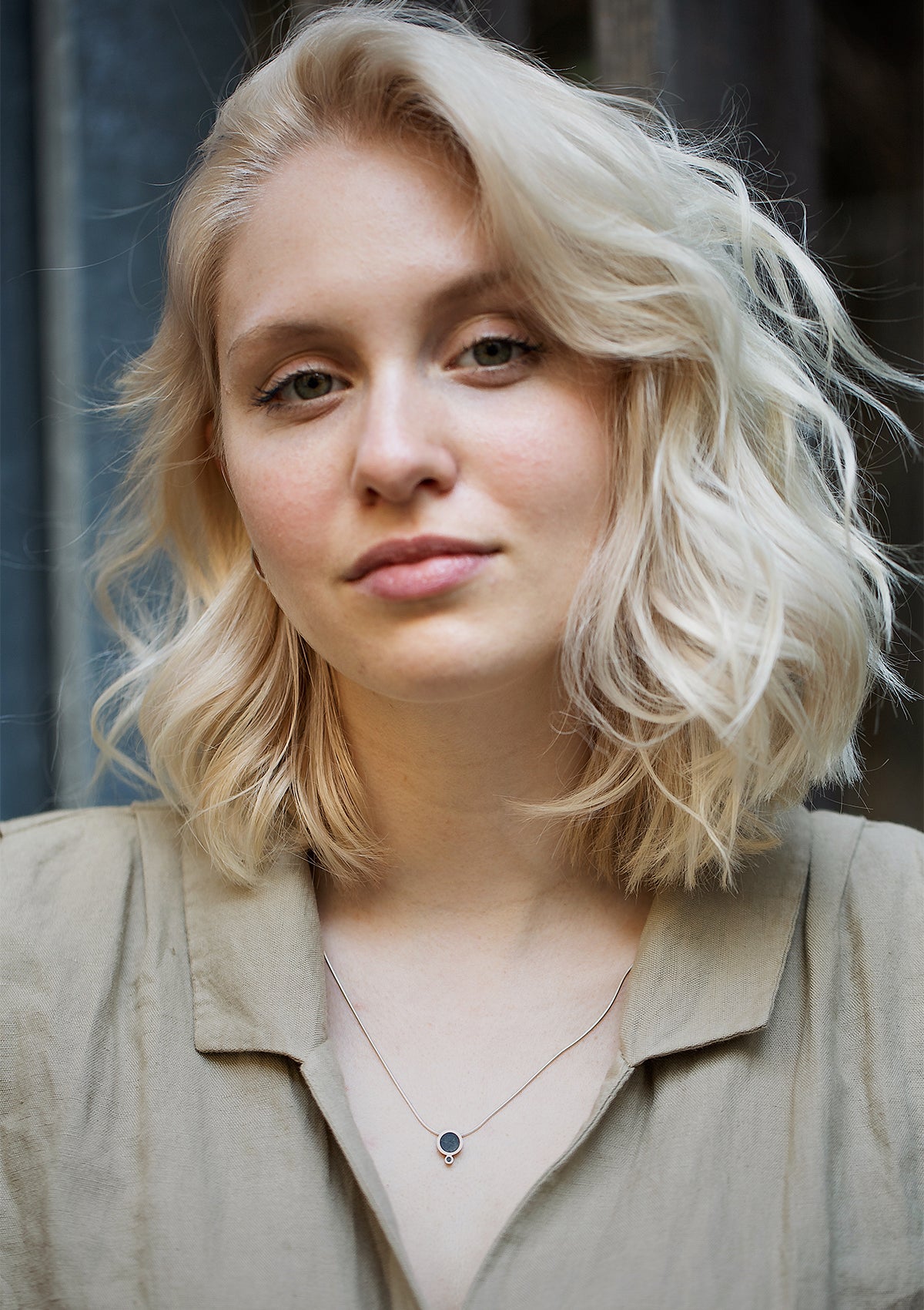 Blonde model in beige shirt wearing silver and concrete necklace, soft contrast with rough pendant texture