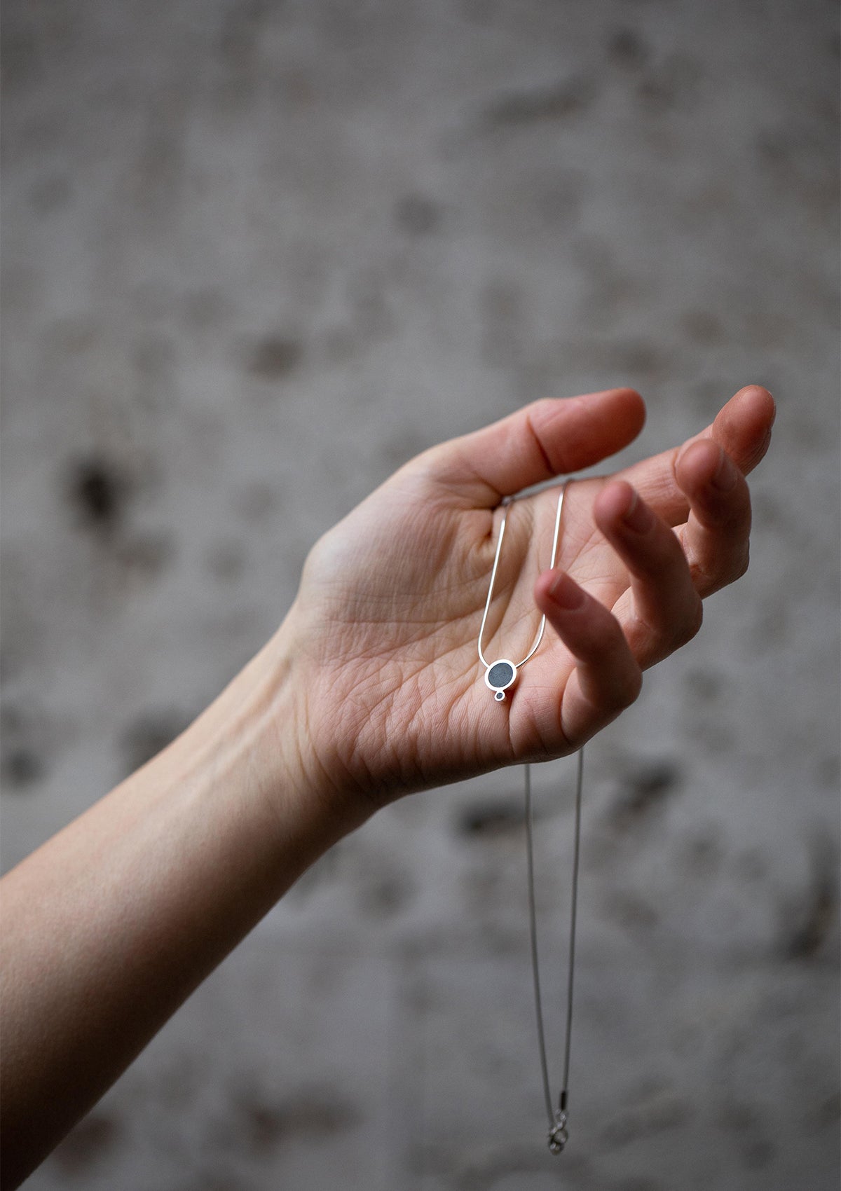 Sterling silver geometric necklace held in hand, showcasing small and large circles with matte concrete texture