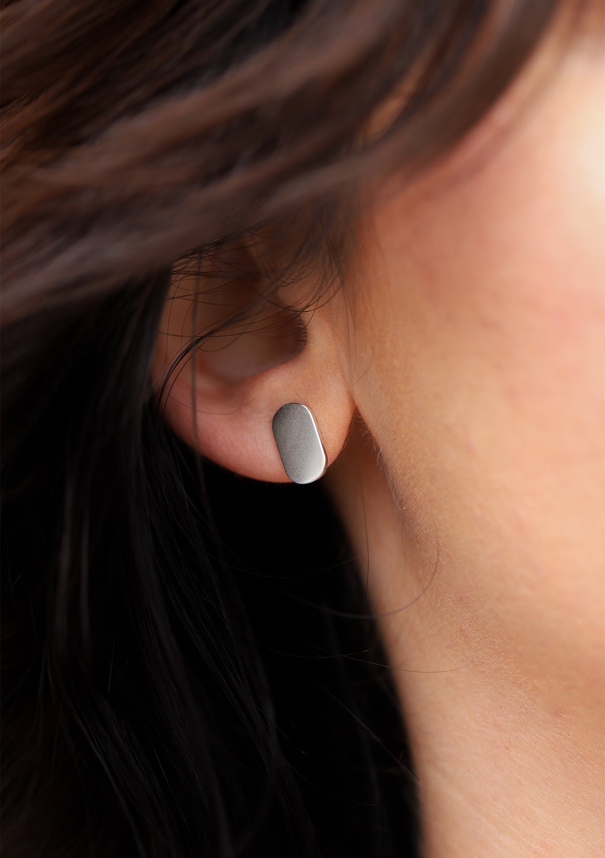 Flat oval silver stud earrings on ear, geometric matte finish, elegant everyday earrings