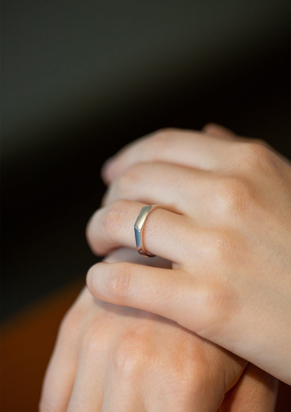 Delicate faceted silver ring worn on finger, reflective angles catching light in soft movement