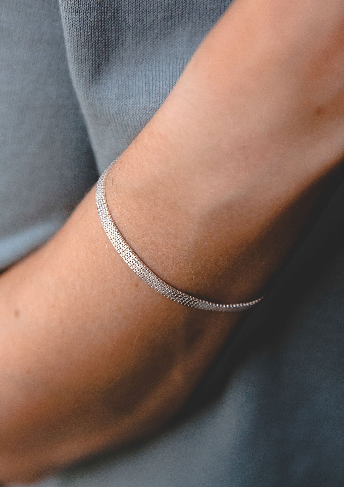 Sterling silver flat chain bracelet on wrist, elegant thin bracelet with subtle sparkle, worn on model's arm